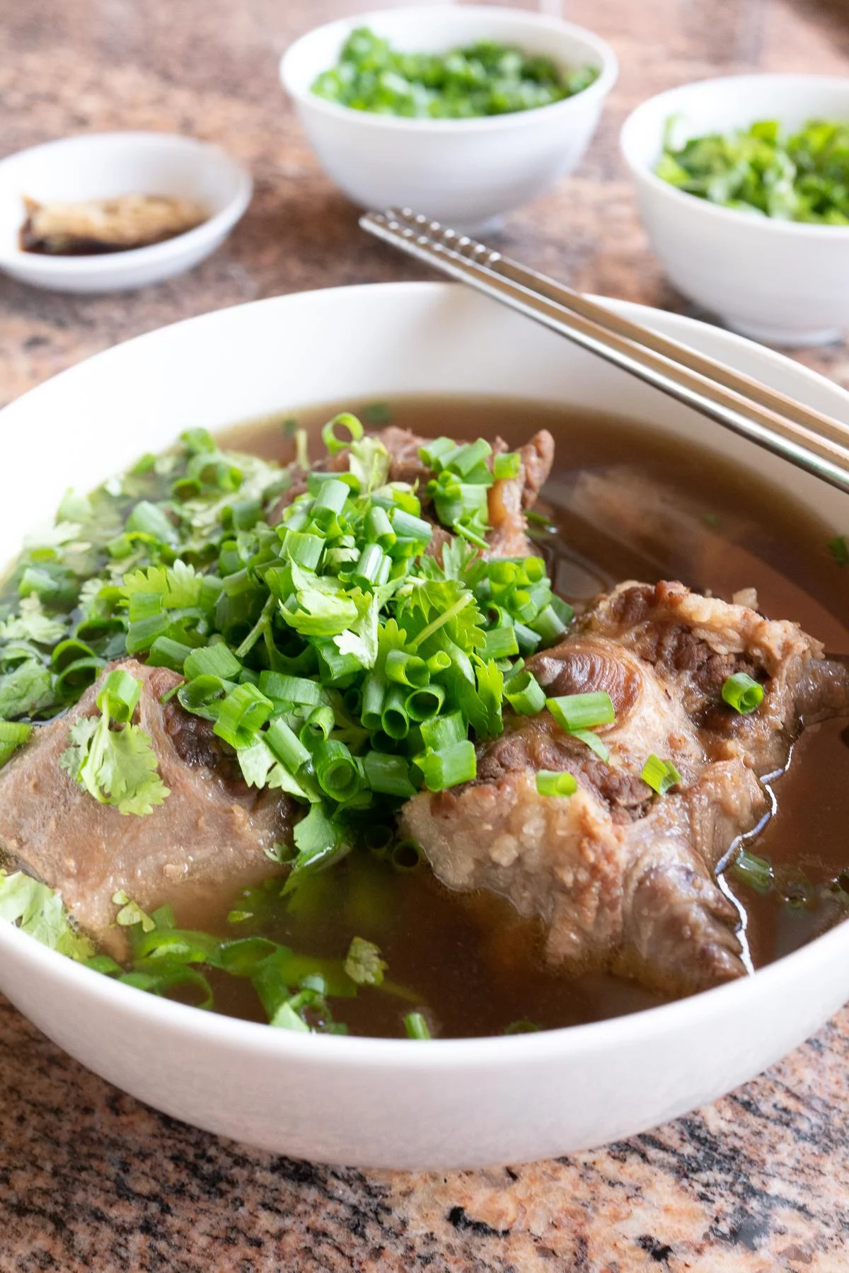 A bowl of oxtail soup with green onions and cilantro sprinkled on top.