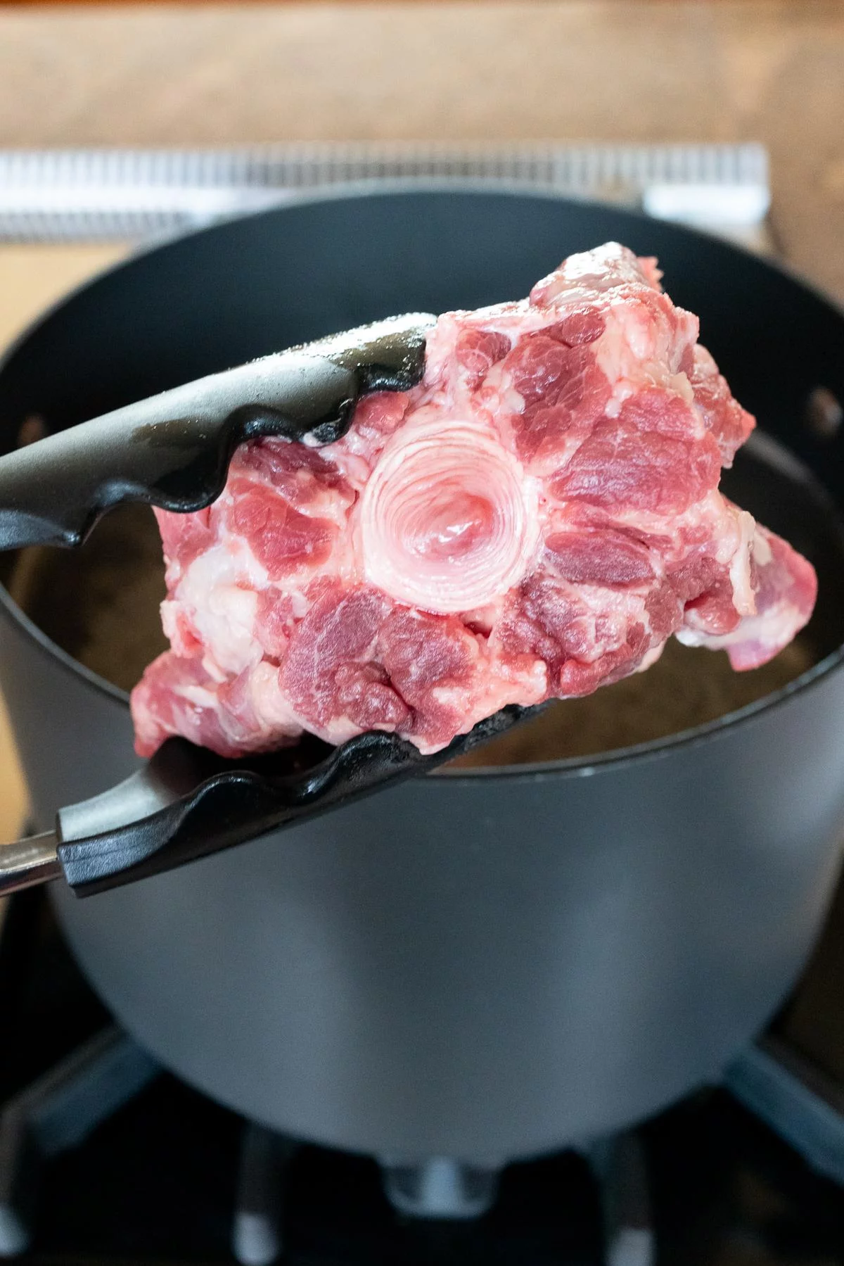 Placing an oxtail into the boiling water to parboil