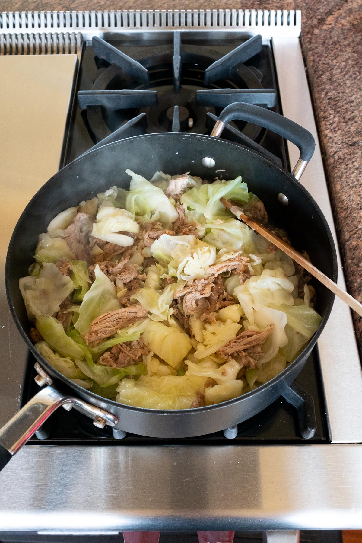 Cooking down the kalua pork and cabbage in a saucepan with kalua pork drippings/juices