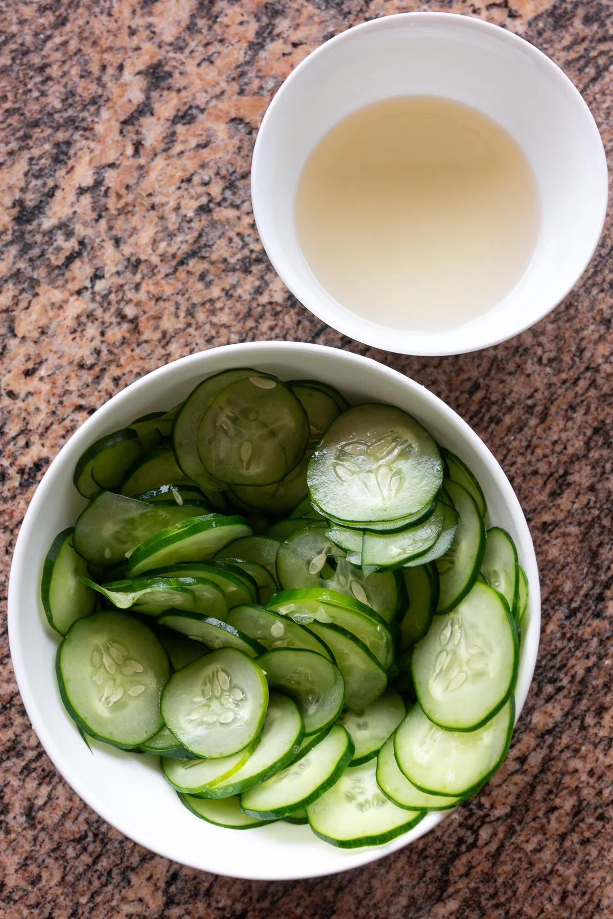 A bowl of salted, thinly sliced Japanese cucumbers. And another bowl with sugar dissolved into rice vinegar.