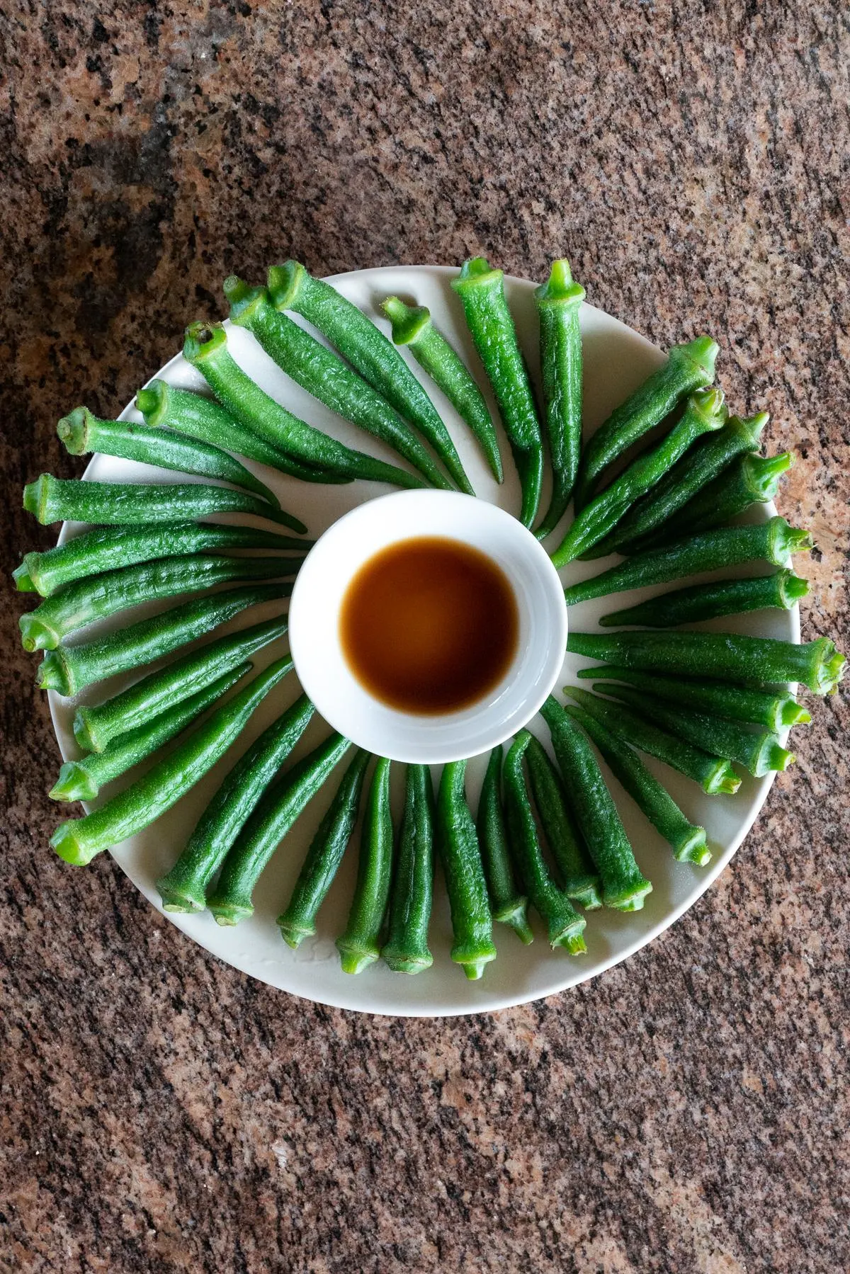 A plate of boiled okra with a small dish of soy sauce for dipping.