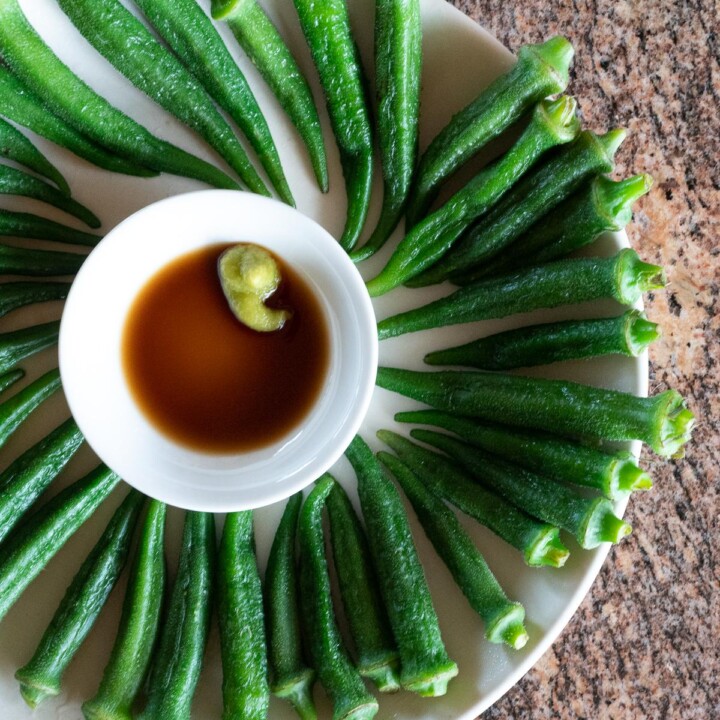 A plate of boiled okra with a small dish of soy sauce and wasabi for dipping.