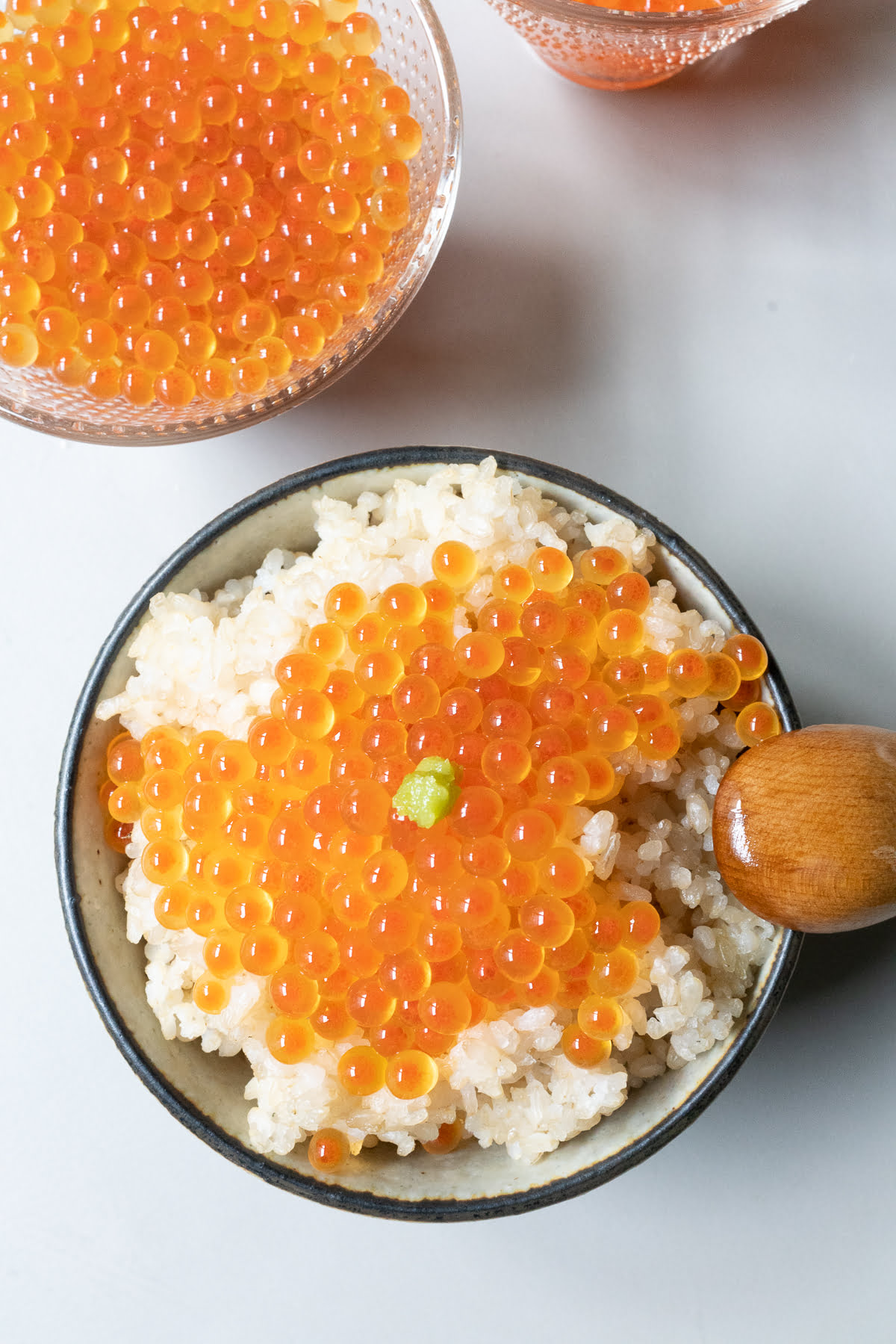 Ikura (soy sauce-cured) salmon roe over a bowl of rice with wasabi
