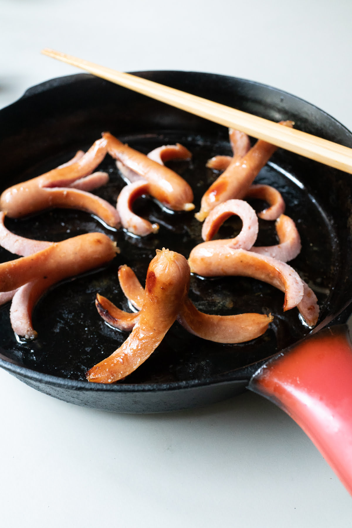 Six cooked Octopus Hot Dogs in a cast iron pan.