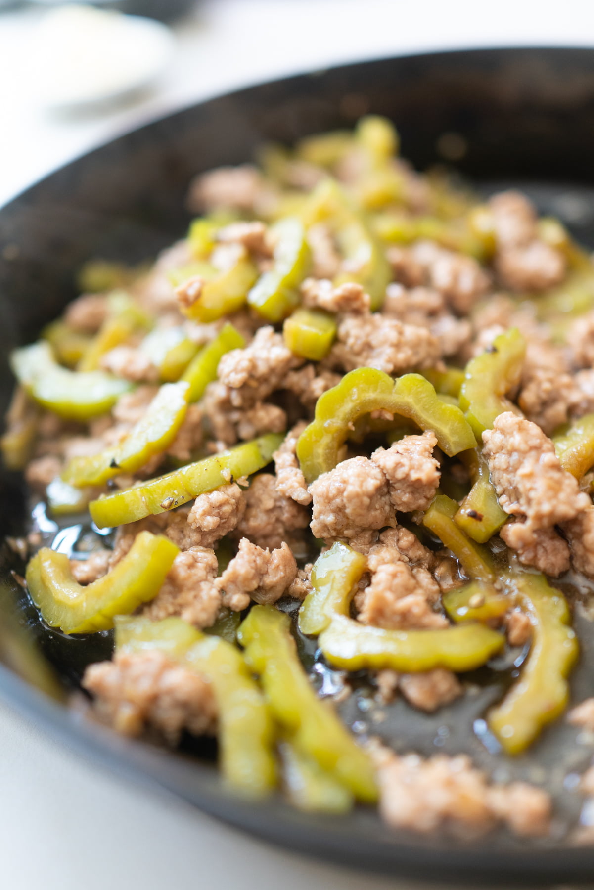 Adding sliced bitter melon to the pan with ground pork.