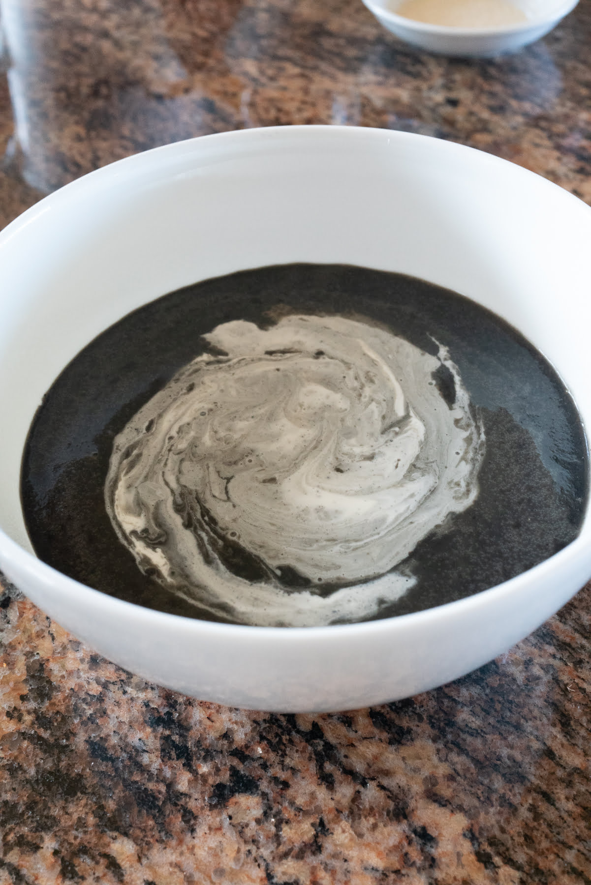 A bowl with black sesame pudding and heave whipping cream being whisked into the bowl.