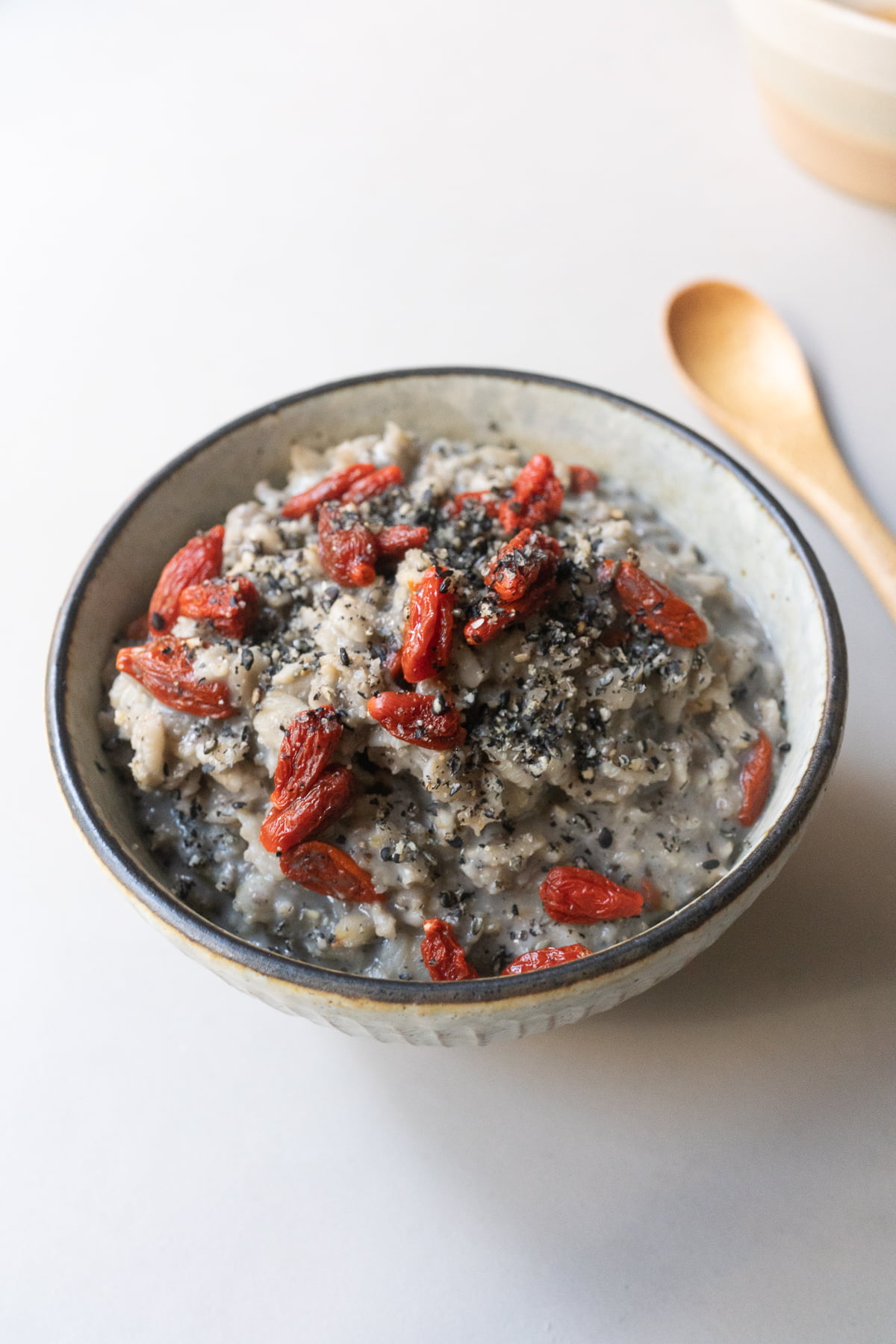 A bowl of almond milk oatmeal with chia seeds, black sesame seeds, goji berries, and honey.