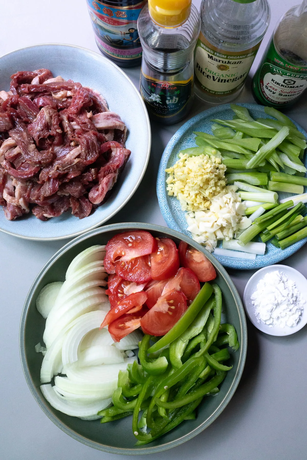 Ingredients for Beef Tomato, laid out on a table (beef, tomato, onions, celery, bell peppers, green onions, ginger, garlic, cornstarch, soy sauce, oyster sauce, rice vinegar, and sesame oil).