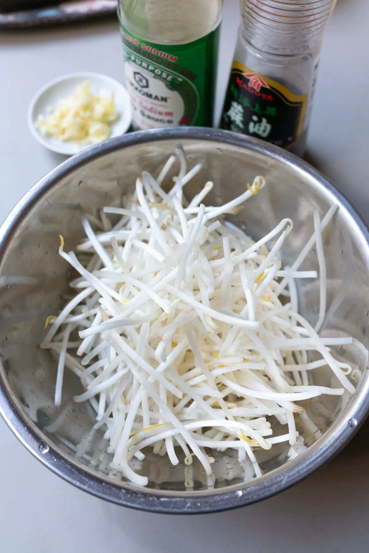 Ingredients for bean sprouts stir fry on a table (bean sprouts, garlic, soy sauce, and sesame oil). Not pictured: green onions and white pepper.
