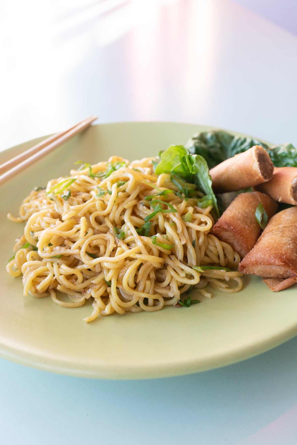 A plate of garlic noodles with a side of lumpia.