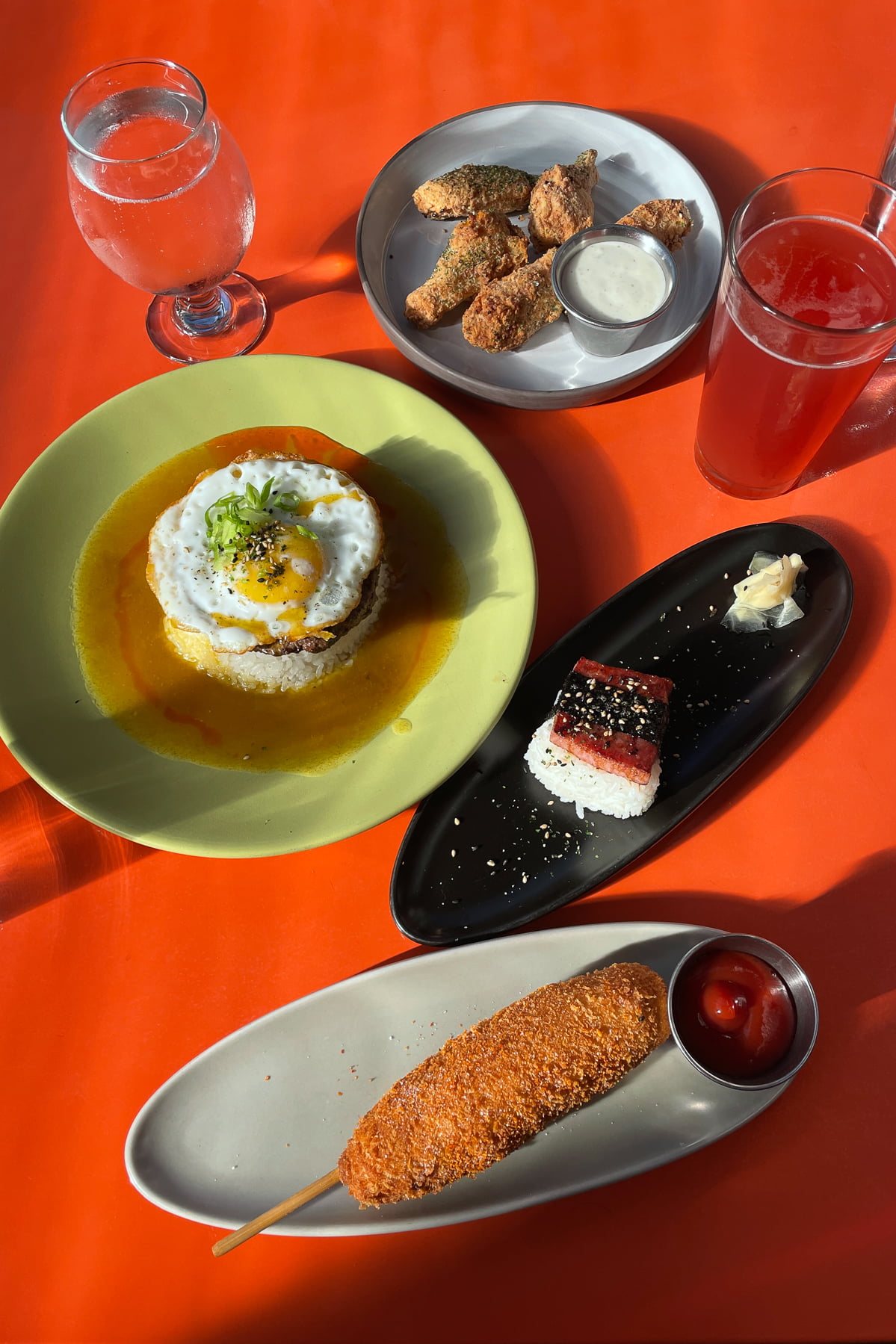 A range of dishes (including Spam musubi, loco moco, and corndog), served at Outer Orbit in San Francisco laid out on a table.