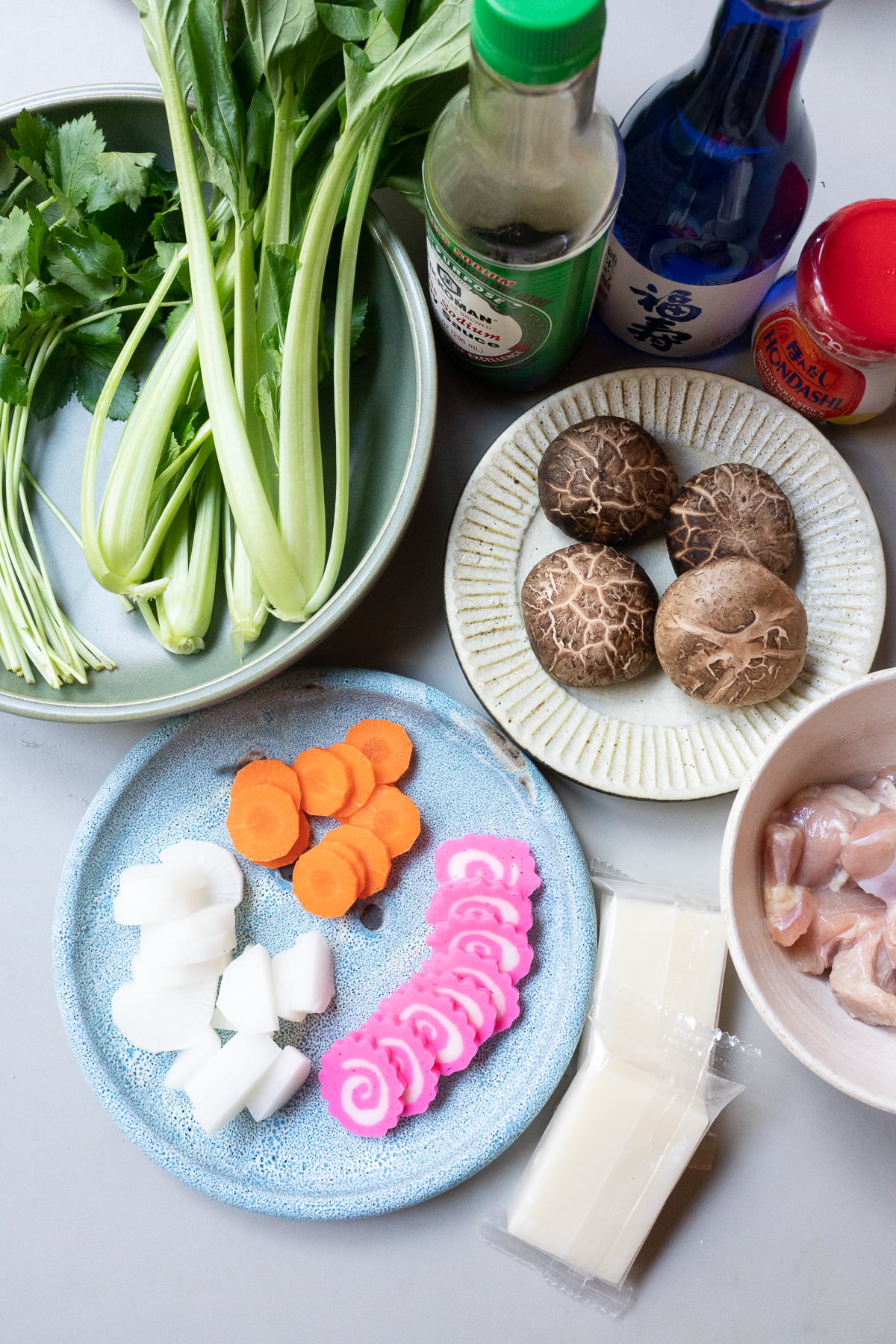 Ingredients for ozoni, laid out on a table (kirimochi, chicken, kamaboko, carrots, daikon, mitsuba, komatsuna, shiitake mushrooms, soy sauce, sake, and dashi.