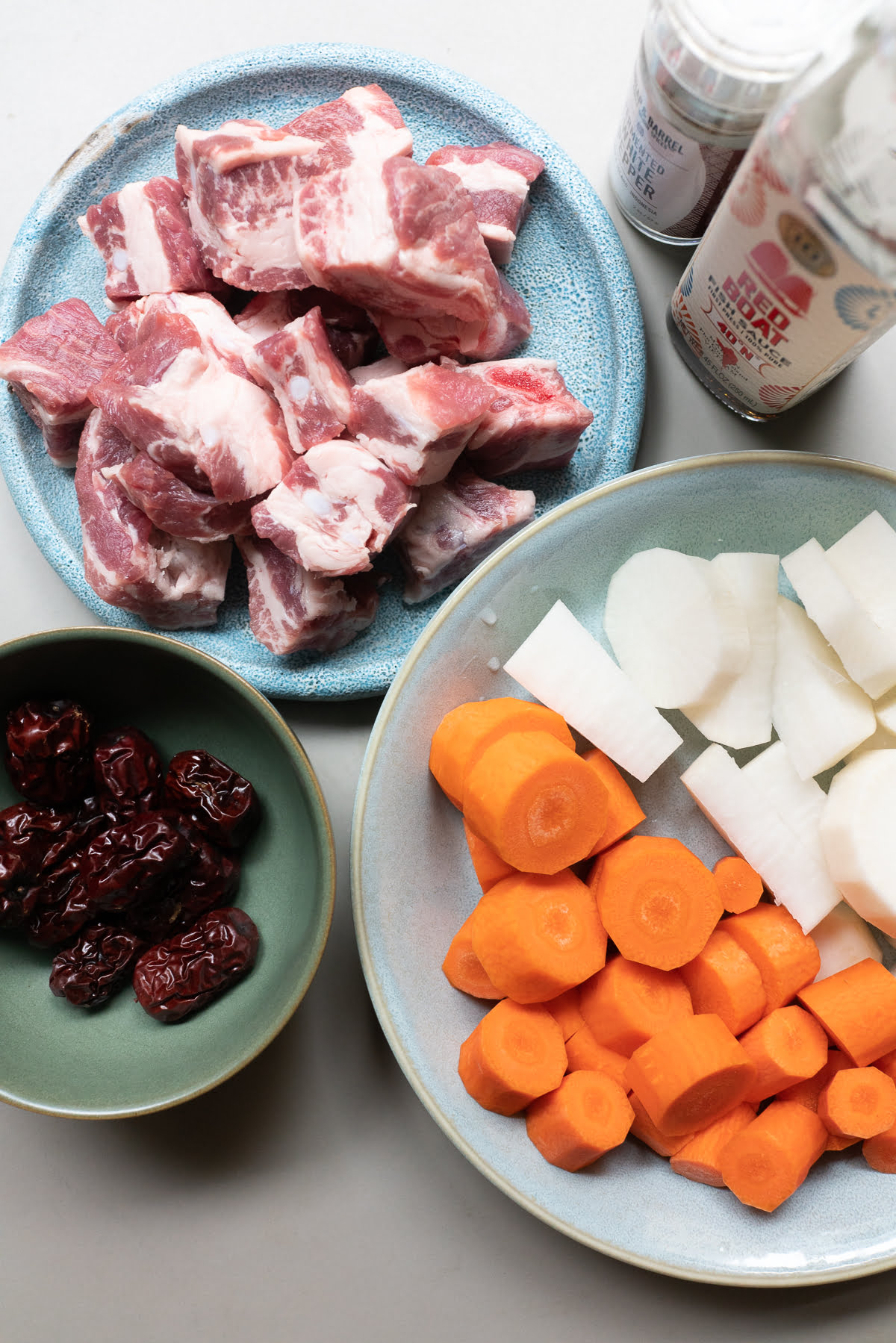 Ingredients for A bowl of Chinese Pork Rib Soup, laid out on a table (pork ribs, red dates, carrots, daikon, fish sauce, and white pepper).