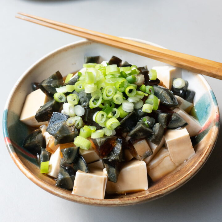 A bowl of silken tofu and diced century eggs with soy sauce, sesame oil, and green onions.