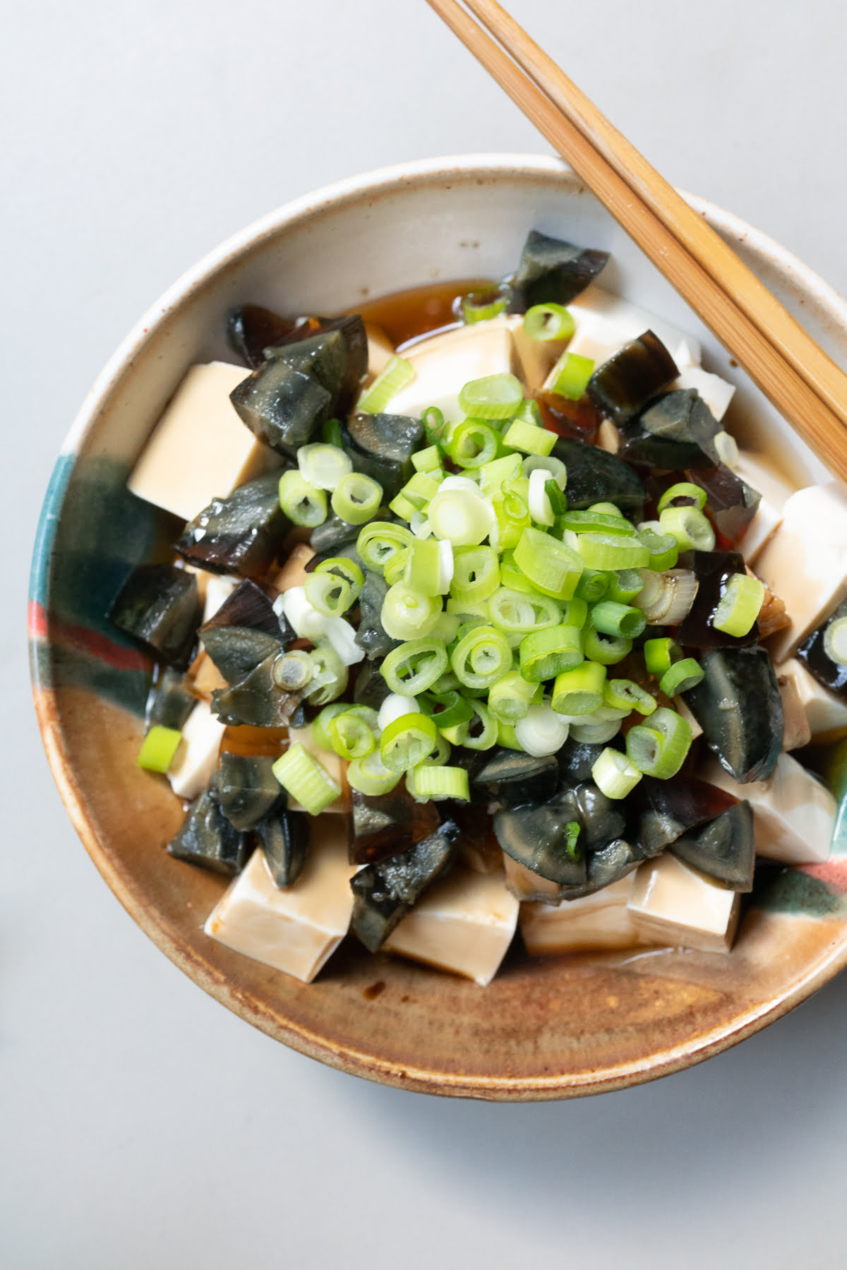 A bowl of silken tofu and diced century eggs with soy sauce, sesame oil, and green onions.