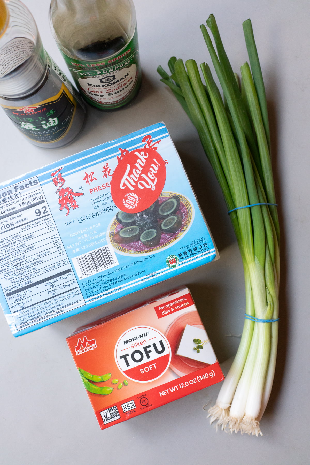 Ingredients for century eggs and tofu on a plate (century eggs, silken tofu, sesame oil, soy sauce, and green onions).