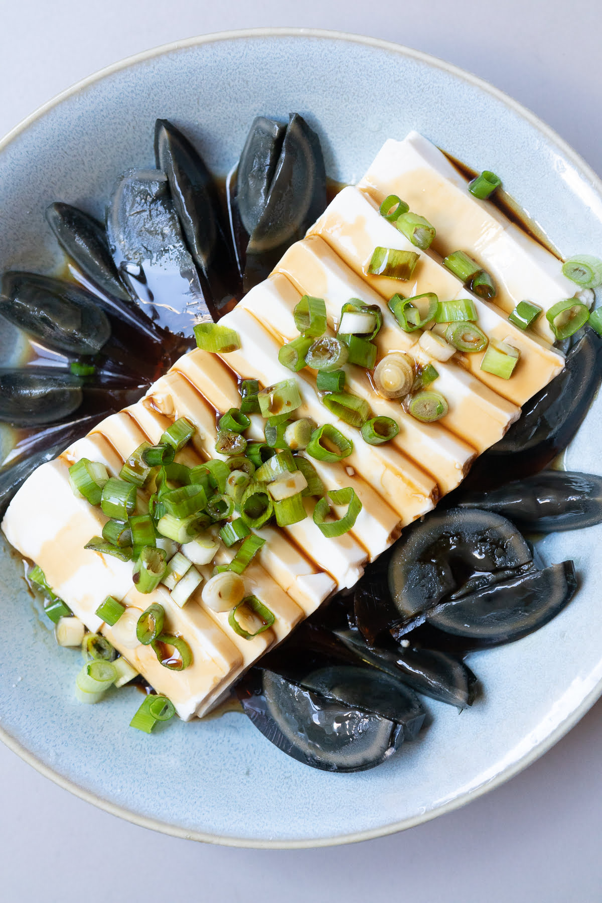 A bowl of silken tofu and sliced century eggs with soy sauce, sesame oil, and green onions.