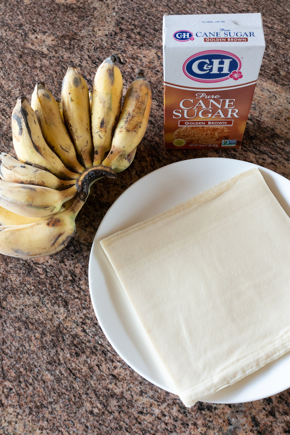Ingredients for banana lumpia on a counter (apple bananas, brown sugar, and lumpia wrappers).