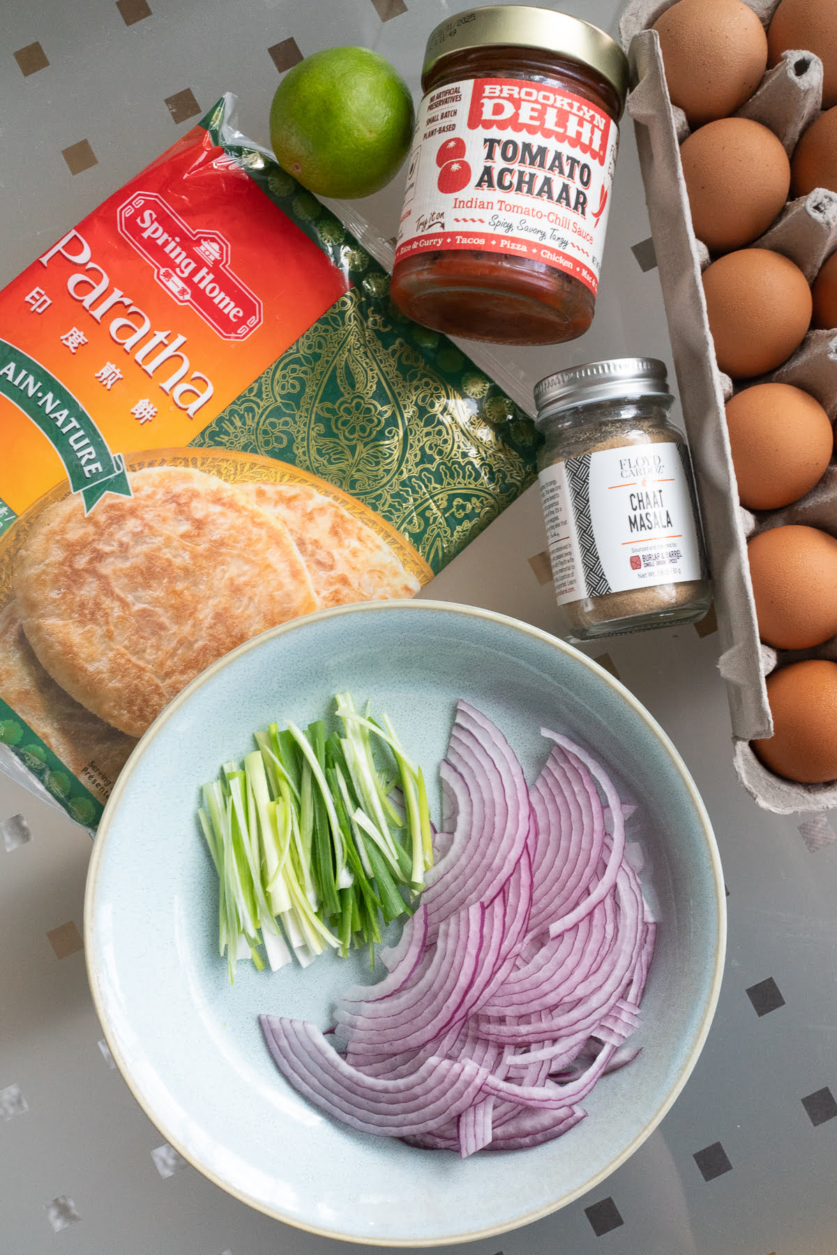 Ingredients for kathi roll on a table (paratha or roti, red onions, green onions, chaat masala, tomato chutney, and eggs).