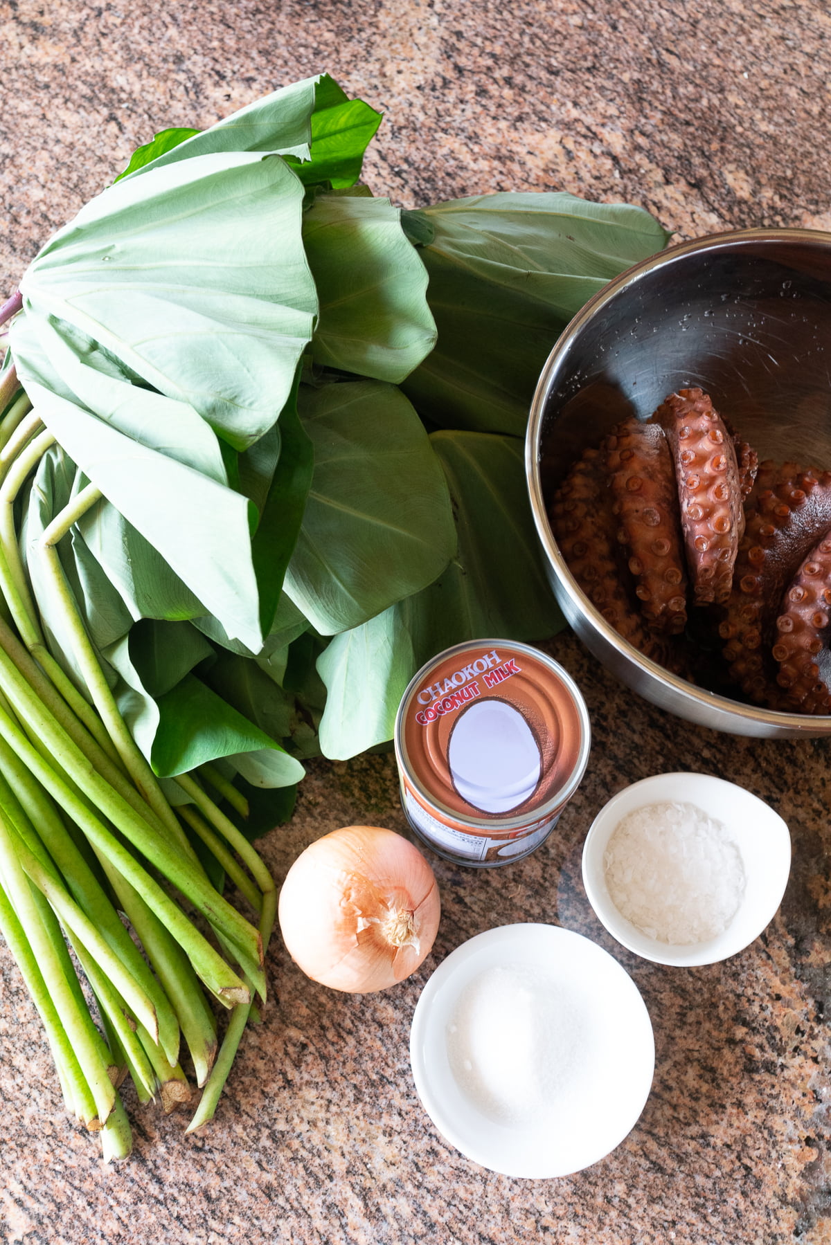 Ingredients for squid luau on a table (luau leaves, tako/octopus which can be used instead of squid, coconut milk, sugar, salt, and onions).