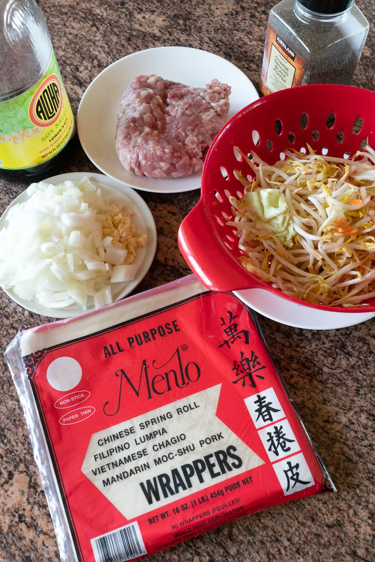 Ingredients for making lumpia on a table (lumpia wrapper, ground pork, onion, vegetable mix, soy sauce, and black pepper).