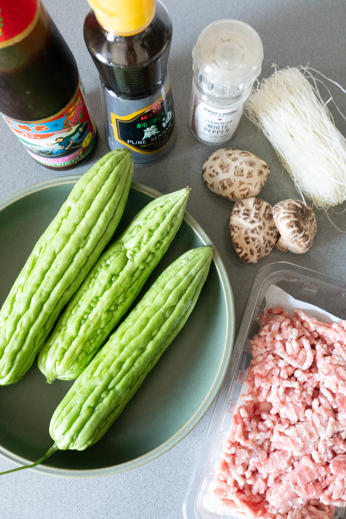 Ingredients for stuffed bitter melon on a table (bitter melon, ground pork, glass noodles, shiitake mushrooms, oyster sauce, sesame oil, and white pepper).