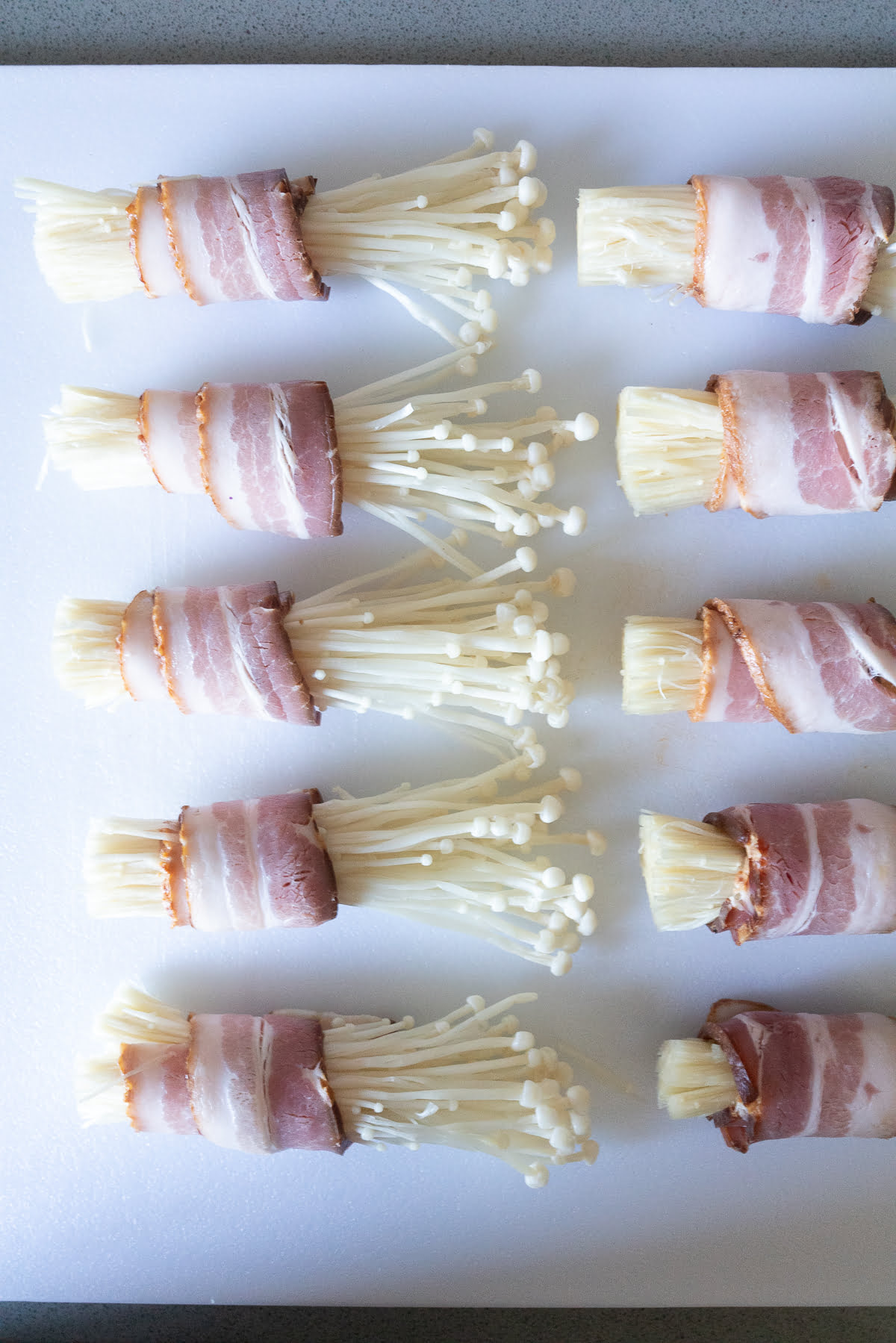 A plate of bacon wrapped enoki mushrooms, ready to be pan fried.