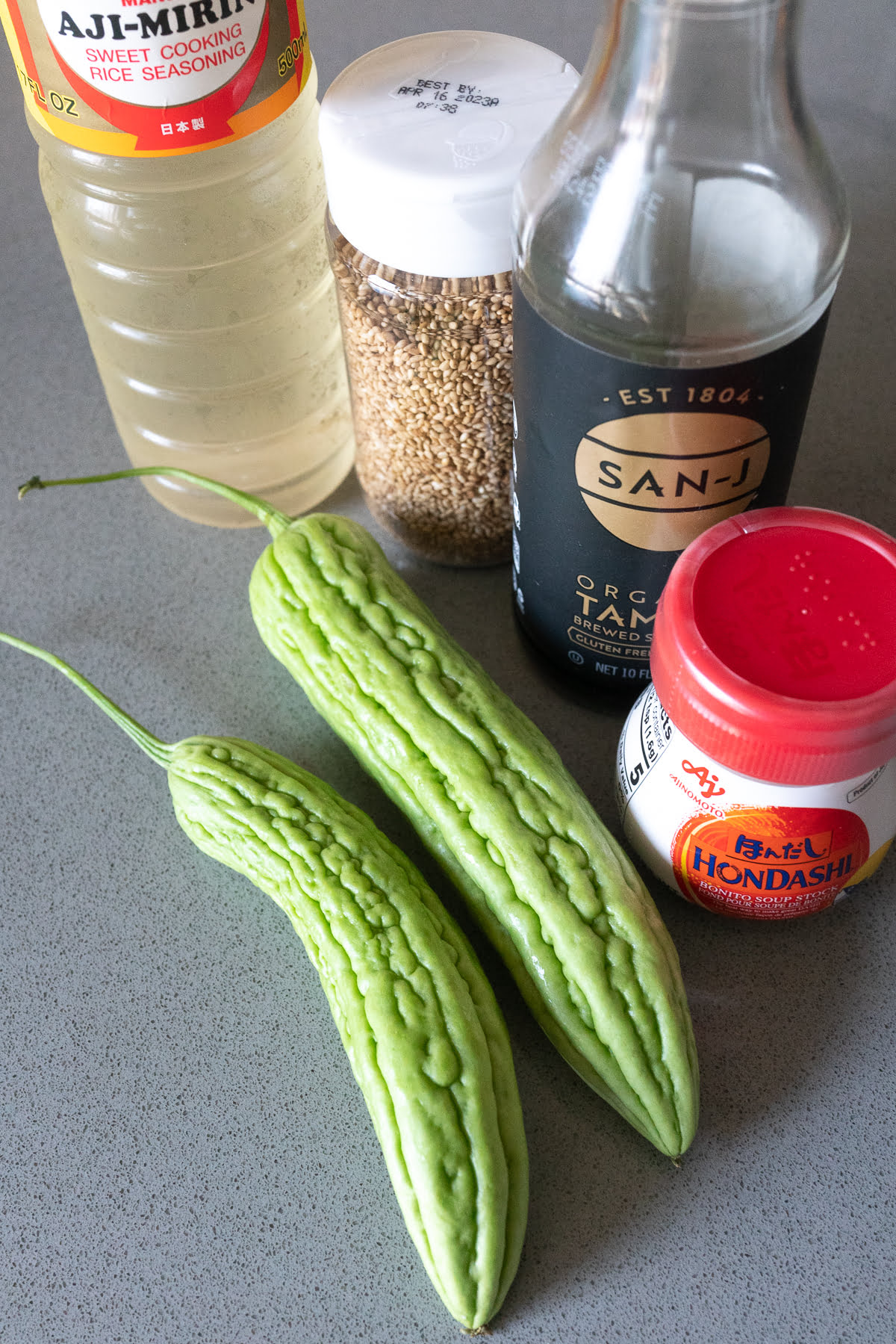 Ingredients for Bitter Melon Tsukudani on a table (bitter melon, mirin, soy sauce, dashi, and sesame seeds).