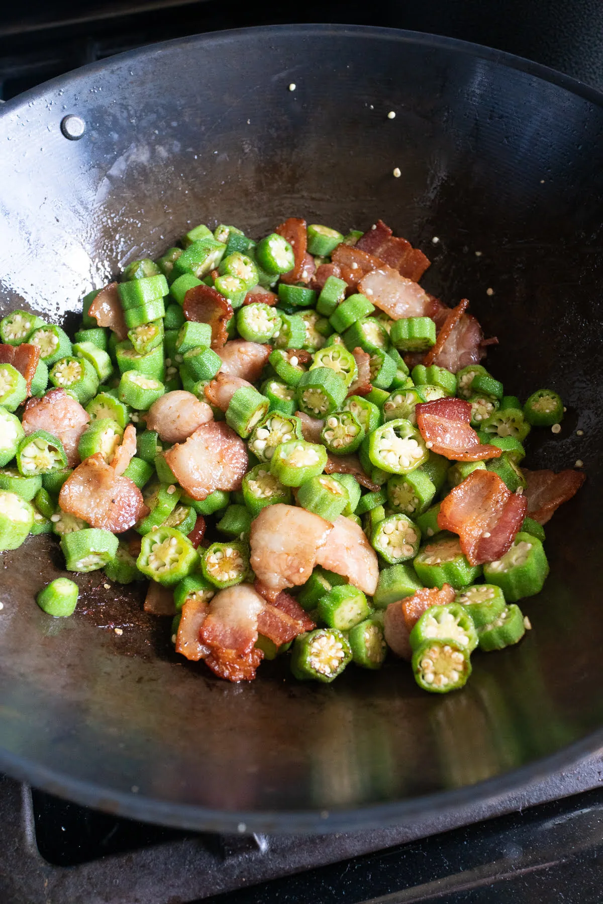 stir frying okra and bacon in a wok.