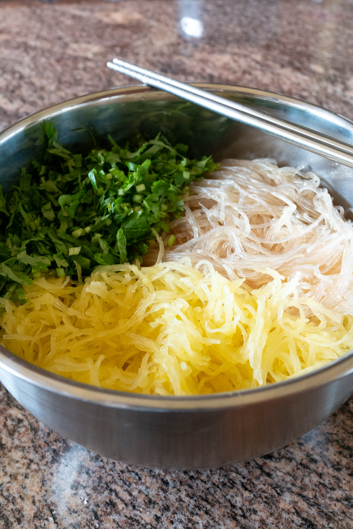 A mixing bowl with roasted spaghetti squash, glass noodles, and cilantro.