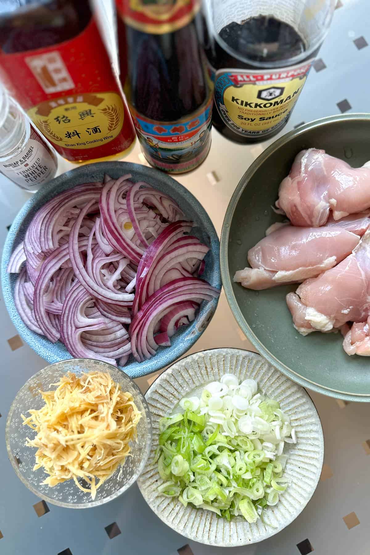 Ingredients for Ginger Chicken laid out on a table (chicken thighs, red onions, ginger, green onions, oyster sauce, soy sauce, Shaoxing wine, and white pepper)