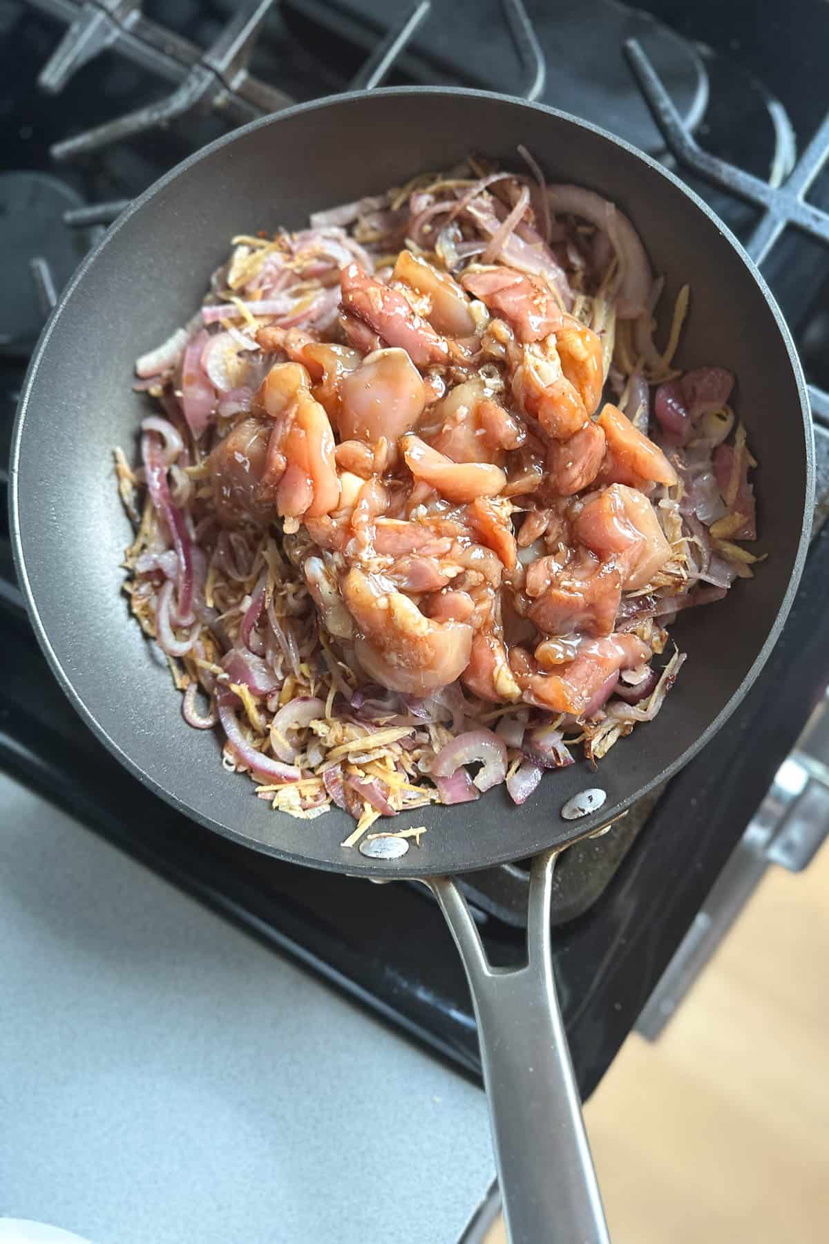 Stir frying marinated chicken thighs with ginger, red onions, and the white parts of green onions.