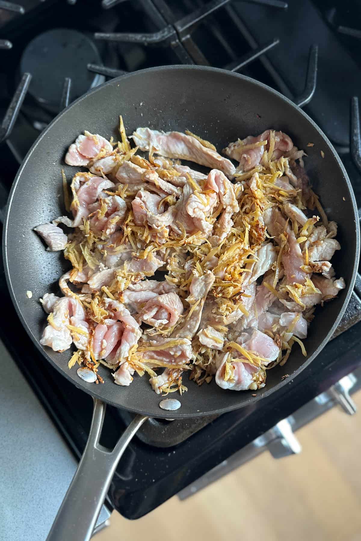 Stir frying the sliced pork with ginger and garlic in a pan.