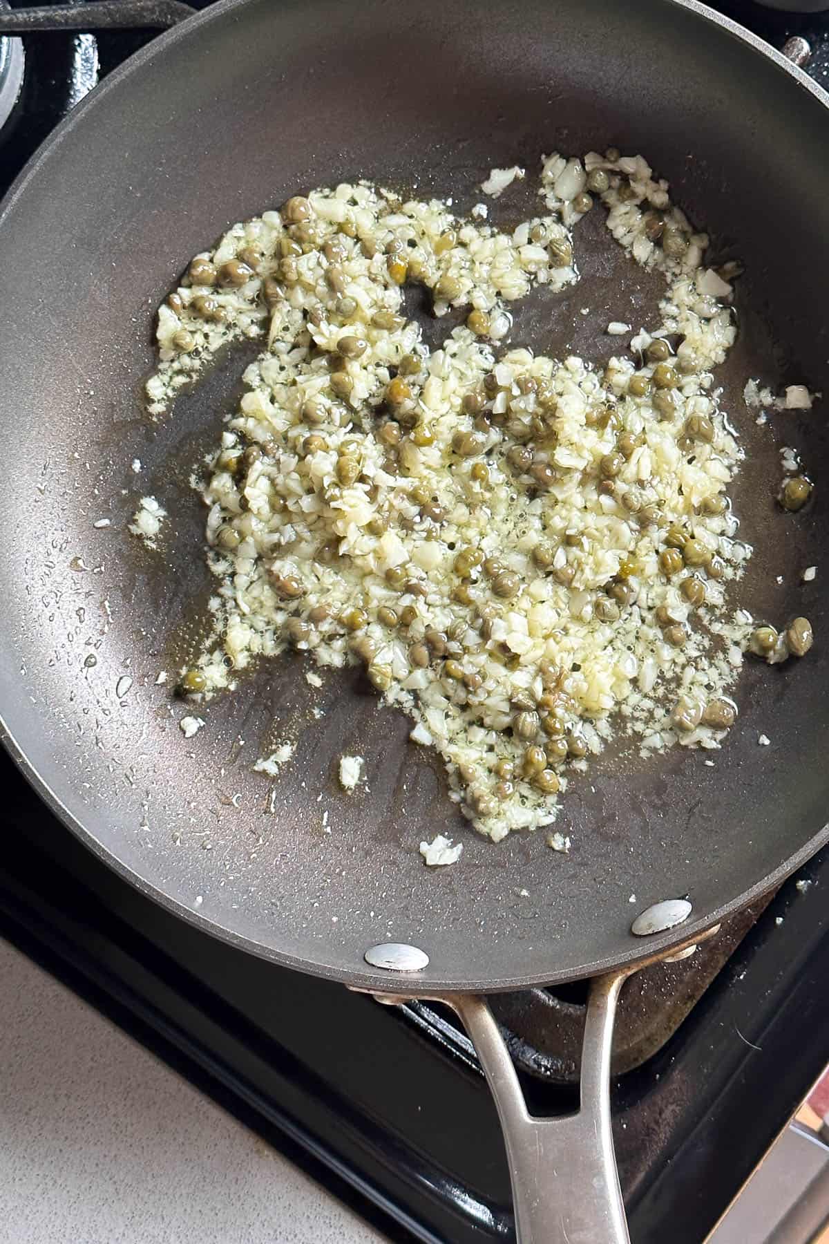 Cooking garlic and capers in a pan.