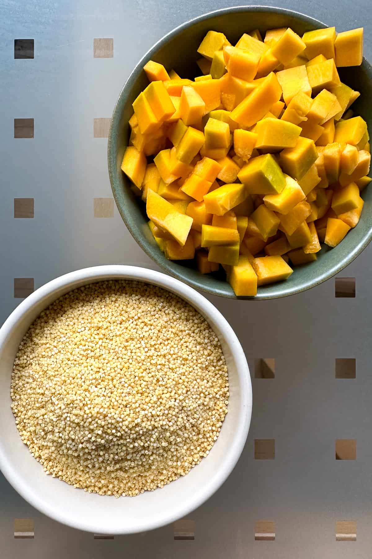 Ingredients for Millet Porridge on a table: a bowl of foxtail millet and a bowl of diced kabocha squash.