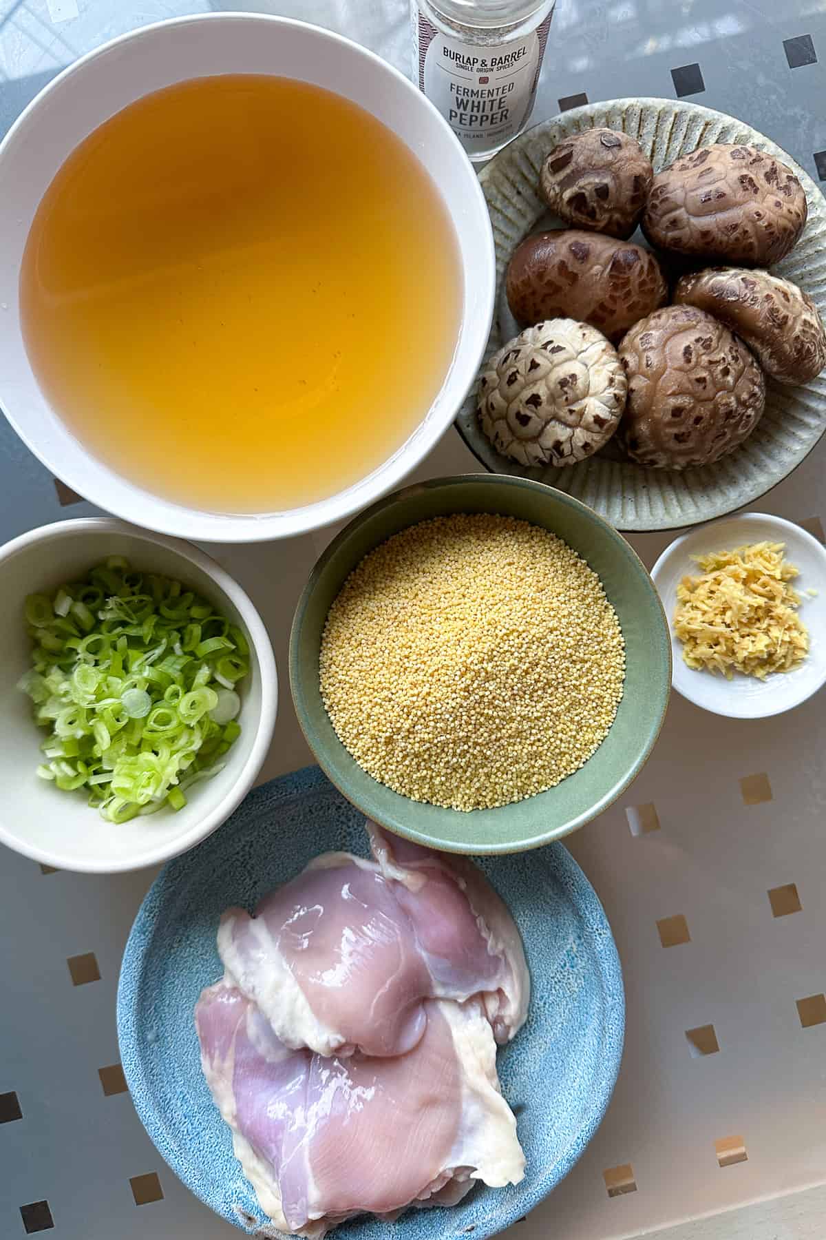 Ingredients for millet porridge with chicken and mushrooms laid out on a table (millet, chicken, mushrooms, mushroom soaking water, green onions, ginger, and white pepper).