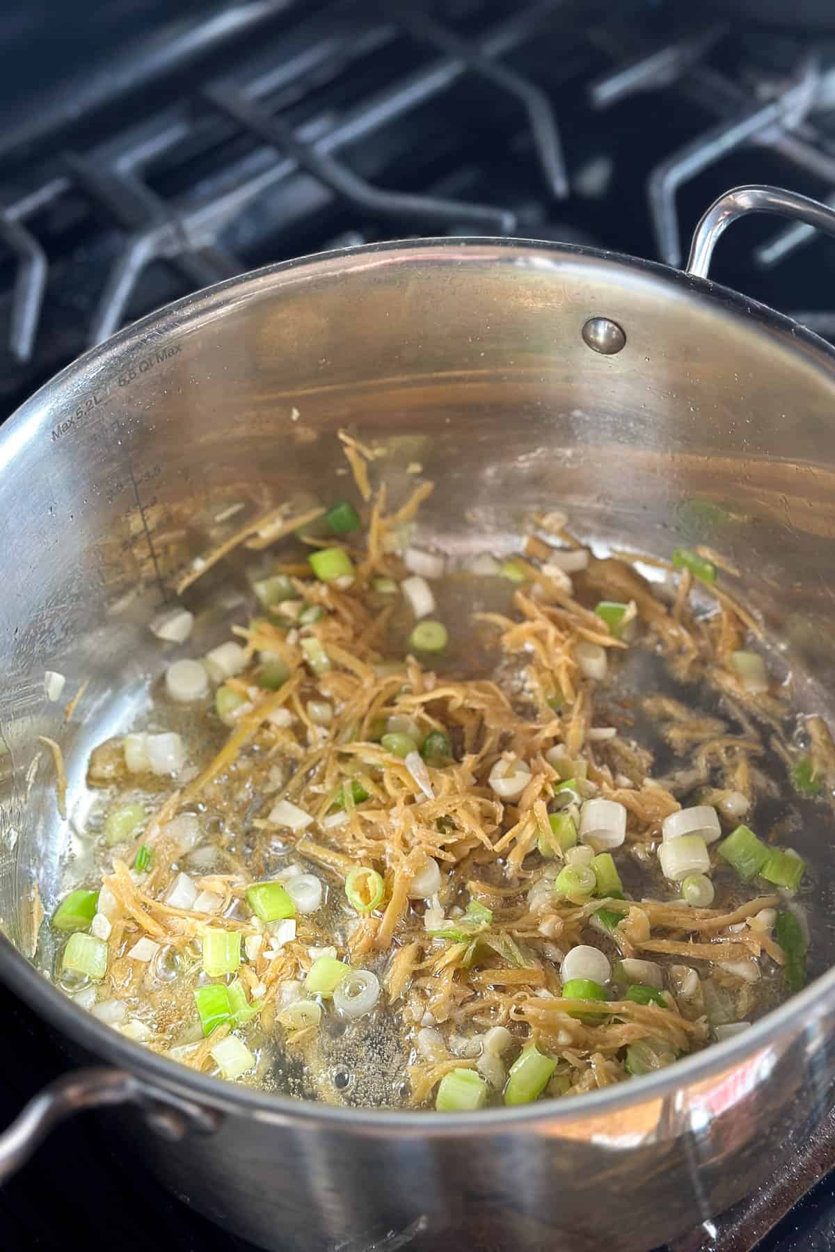 Cooking the ginger, garlic, and green onions in a pot.