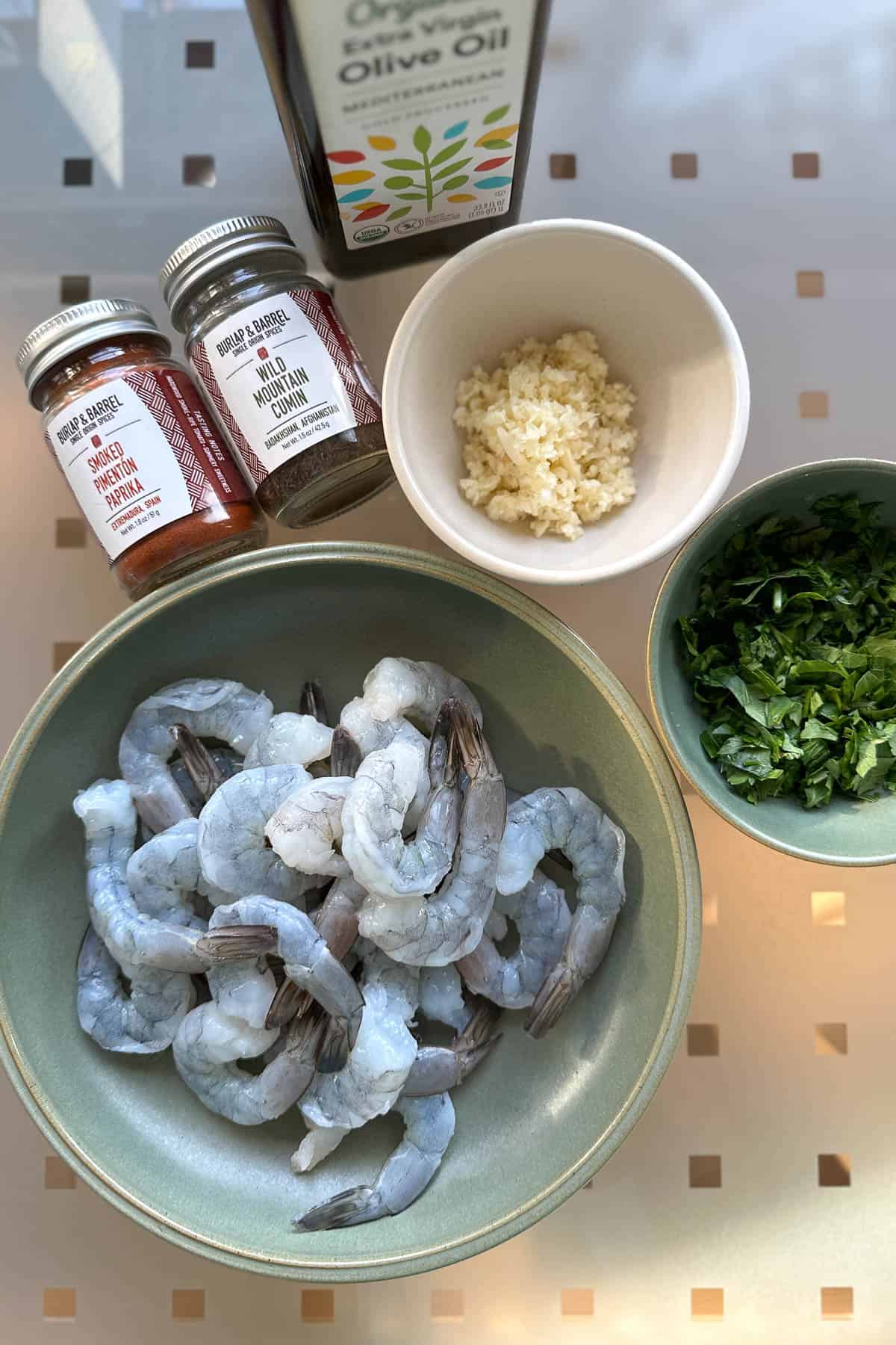 Ingredients for paprika shrimp on a table (shrimp, garlic, parsley, olive oil, cumin and paprika).