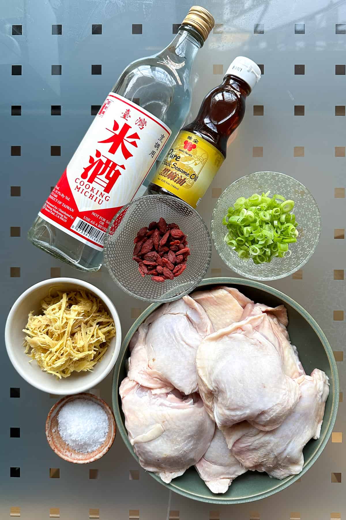 Ingredients for Sesame Oil Chicken Soup laid out on a table (chicken thighs, Taiwanese rice wine, black sesame oil, ginger, salt, green onions, and goji berries)