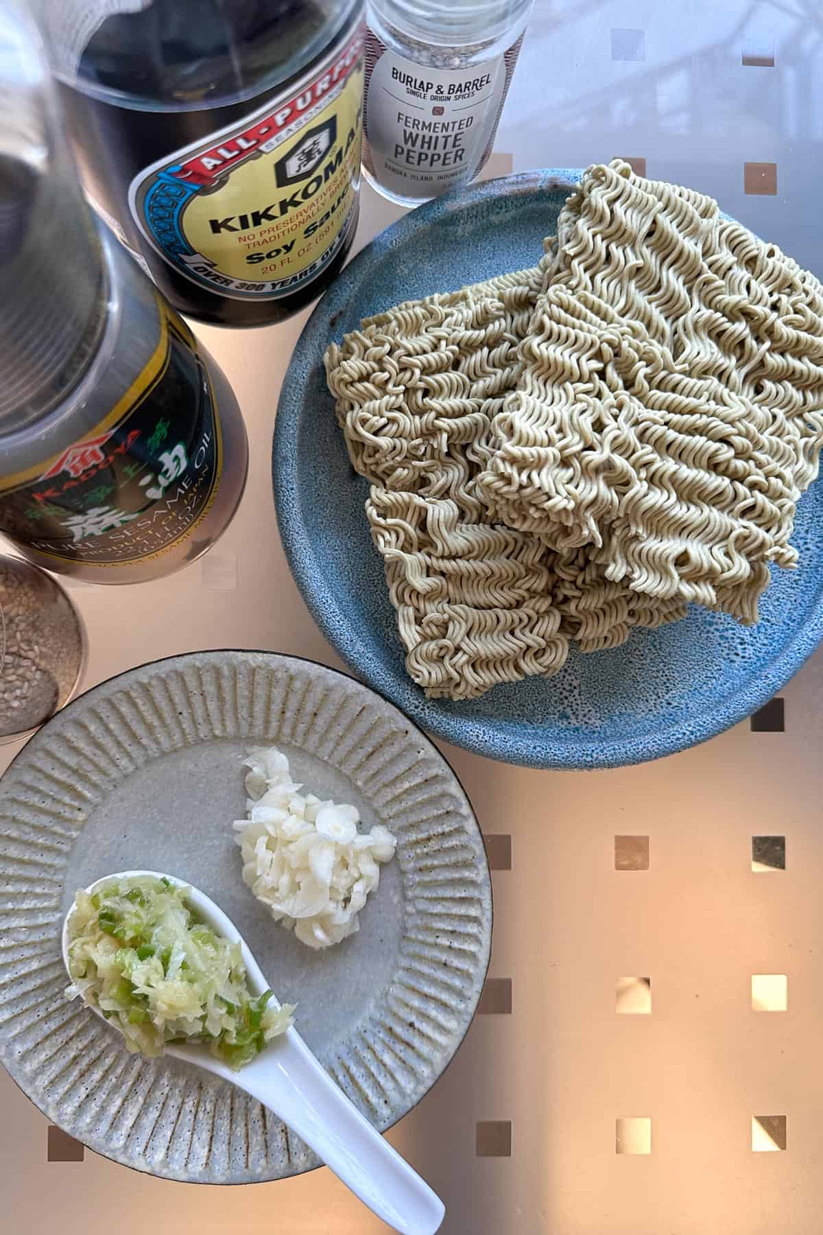 Ingredients for Ginger Scallion Noodles laid out on a table (instant noodles, ginger scallion sauce, garlic, soy sauce, white pepper, sesame seeds, dashi, and sesame oil).