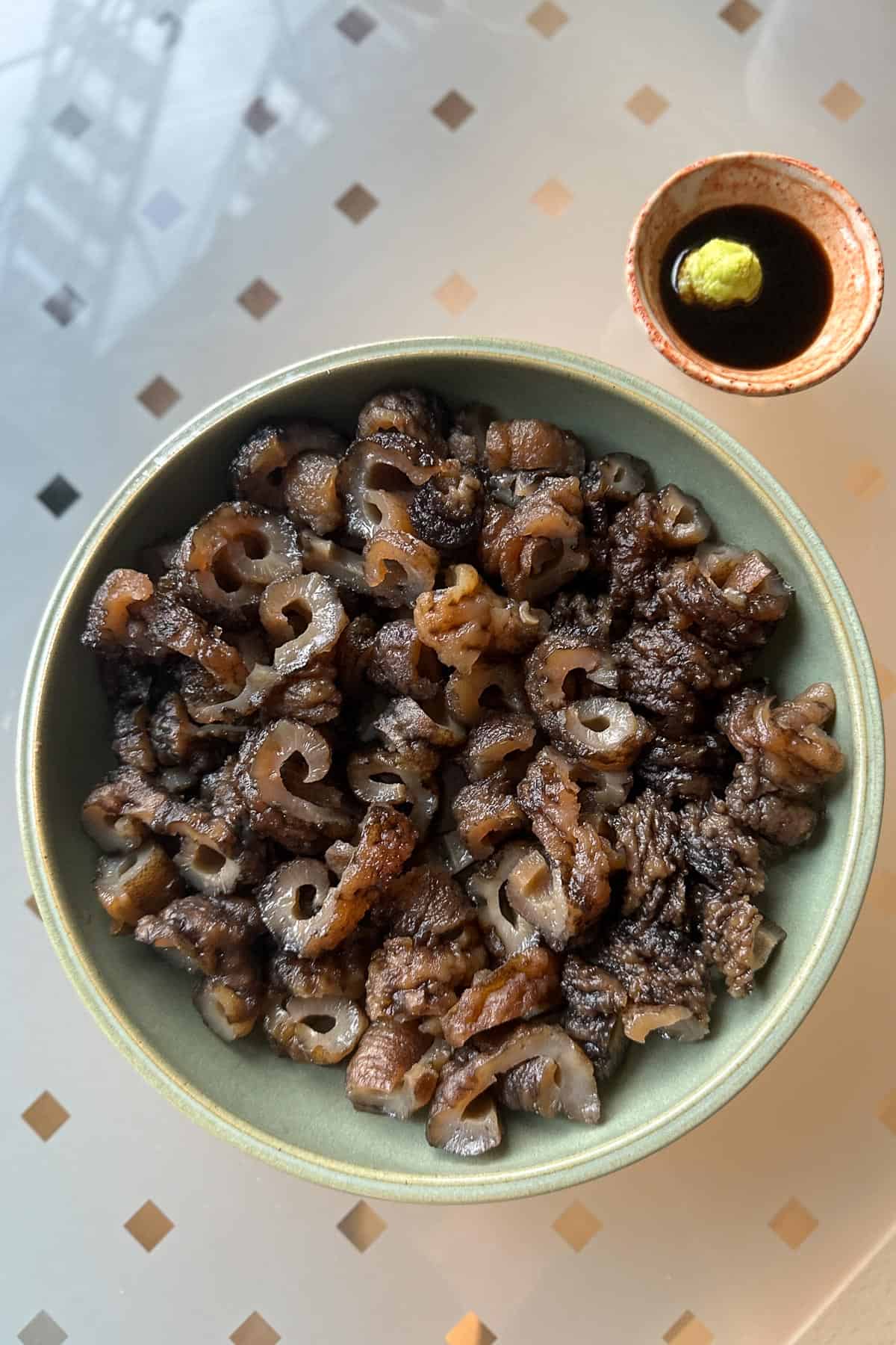 Sea cucumber sashimi on a plate with a side of soy sauce and wasabi for dipping.