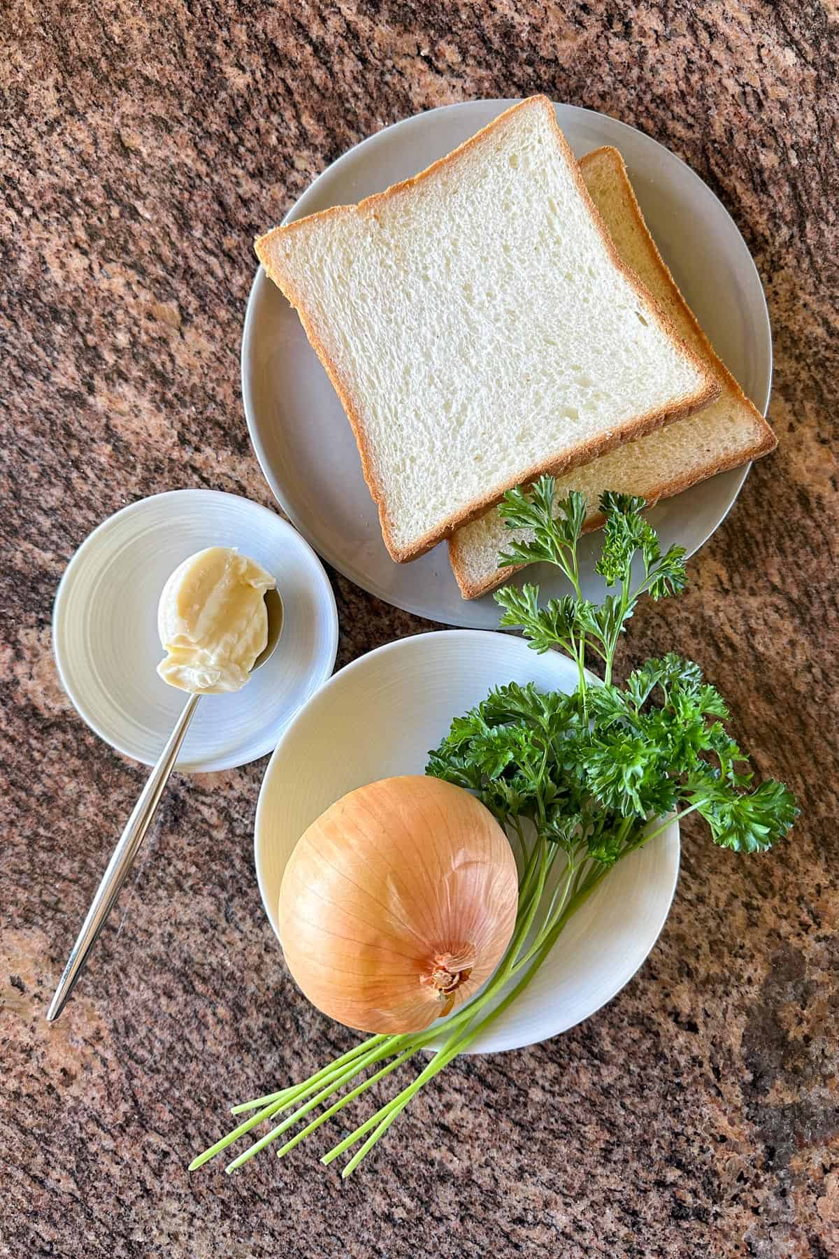 Ingredients for onion sandwich on a table (bread, onions, parsley, mayo).