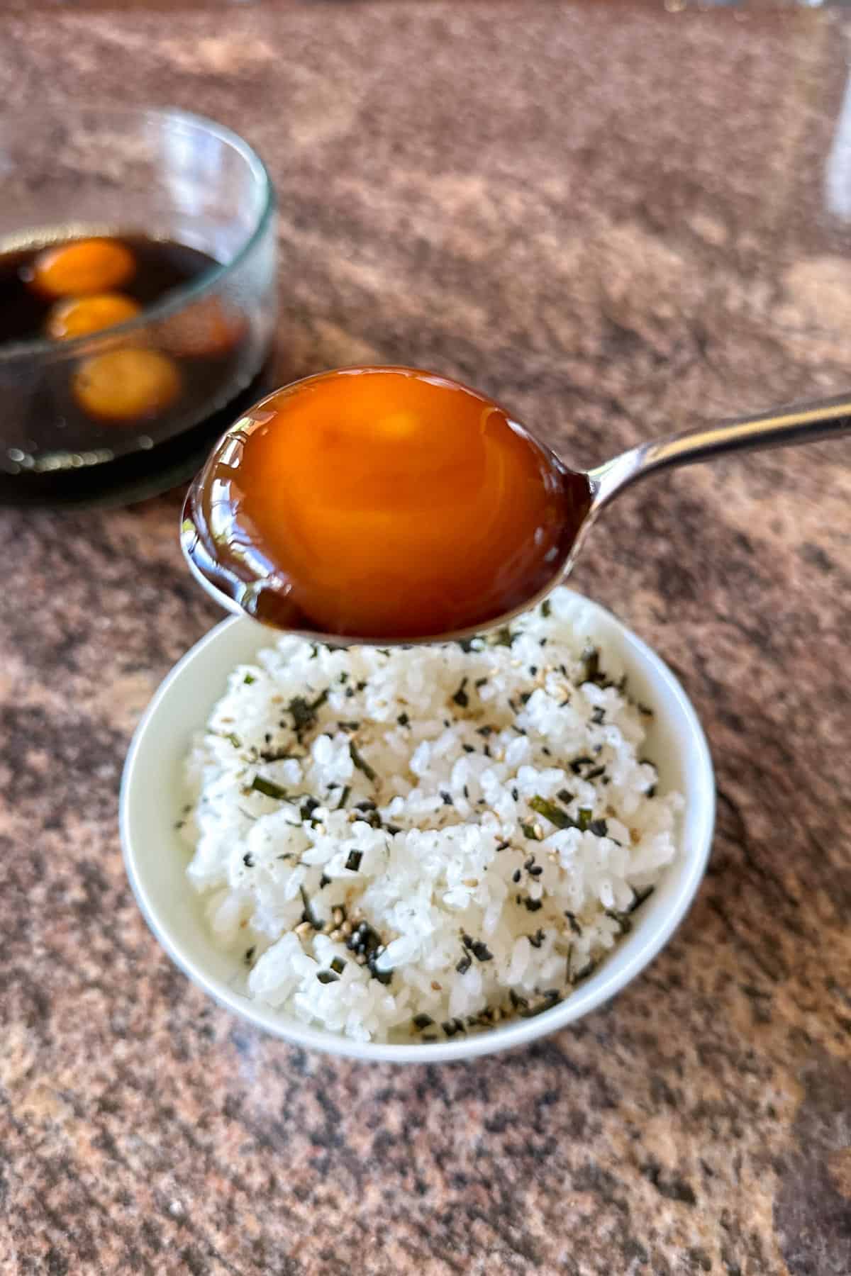 Placing a Soy Cured Egg Yolk on a bowl of rice.