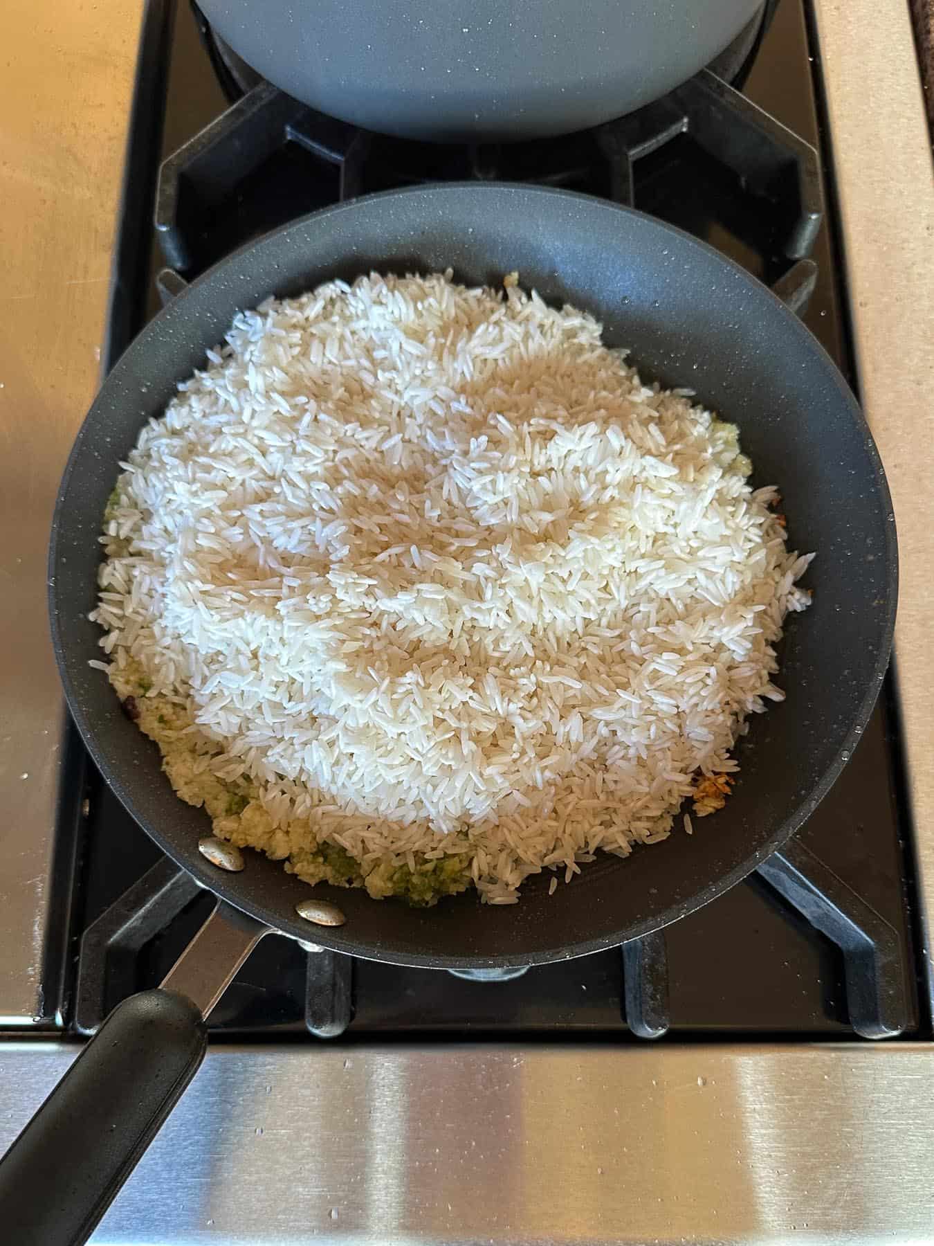Adding jasmine rice to chicken fat, ginger scallion sauce, and minced garlic in a skillet.