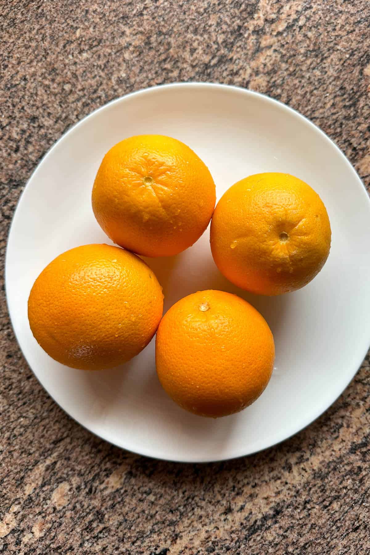 Four oranges on a plate.