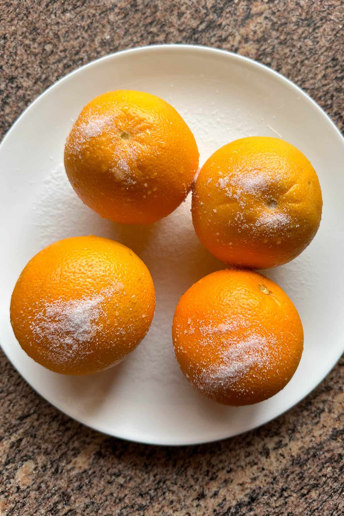 Four oranges (sprinkled with salt) on a plate.