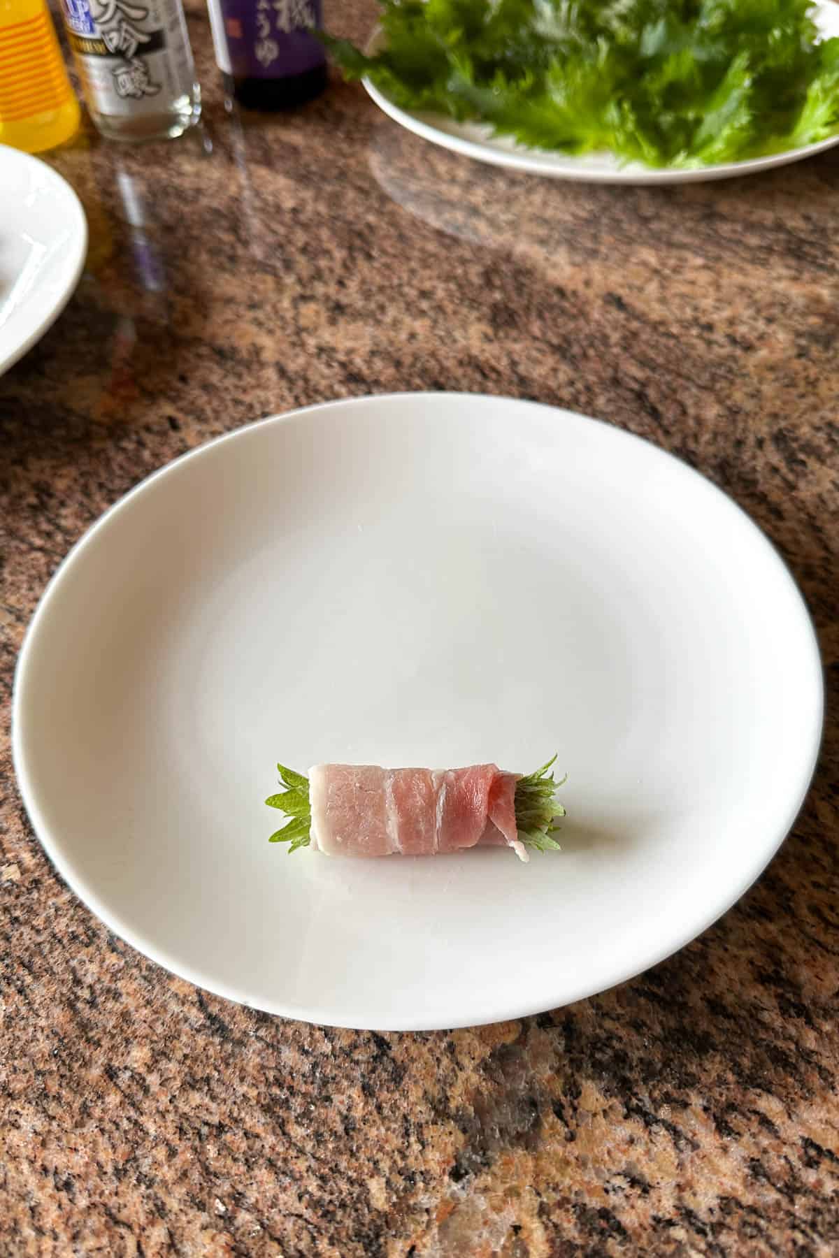 Rolling up pork belly and shiso leave on a plate.